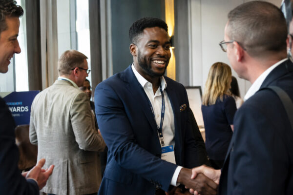Smiling man in a navy blazer shaking hands while networking at a professional business conference.