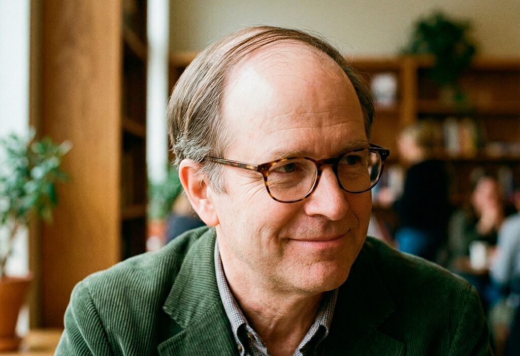 Middle-aged man indoors with thinning comb-over hairstyle, glasses, and green corduroy blazer.