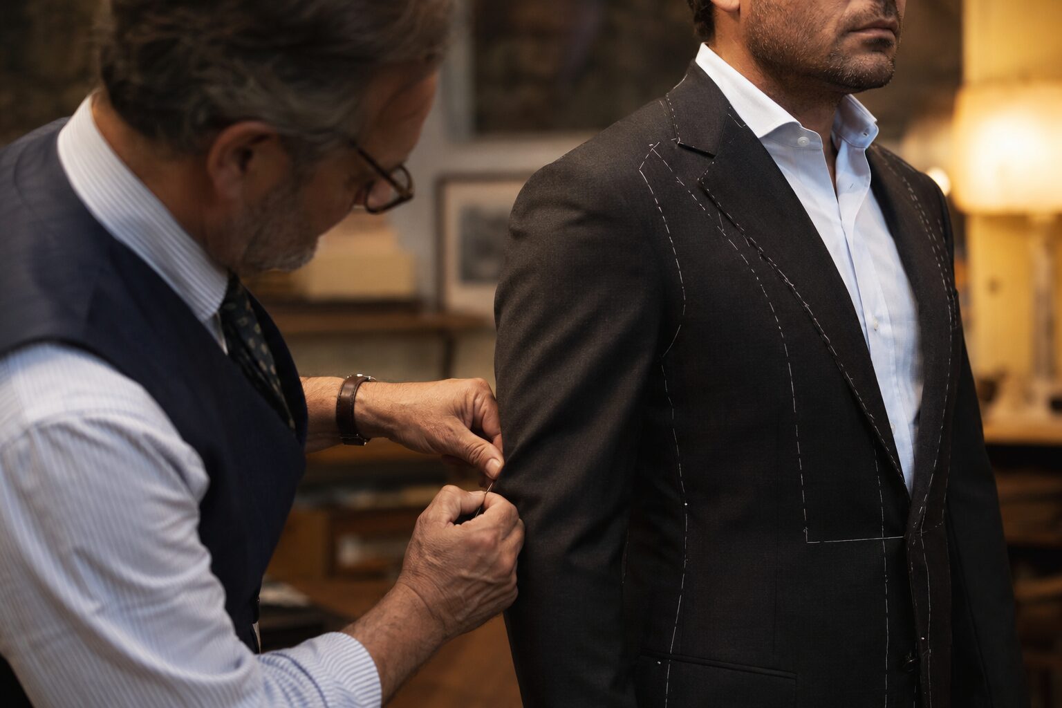 tailor pinning the side seam of a charcoal suit jacket on a compact, muscular man in his early 40s