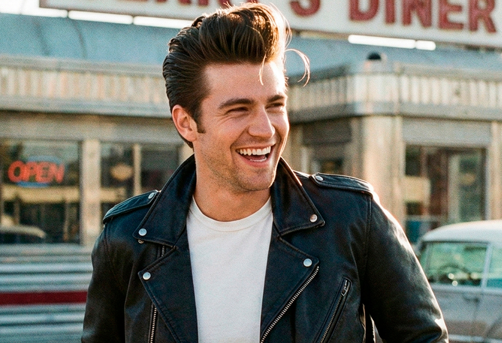 Man wearing pompadour hairstyle and black leather jacket, laughing in retro diner setting