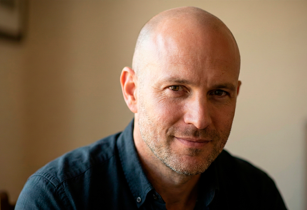 Bald man with light stubble in dark shirt, relaxed smile, clean masculine look