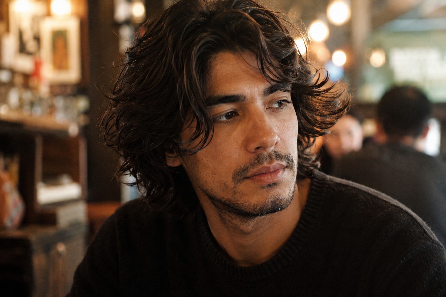 Man with medium-length wavy hair wearing a natural, relaxed style in a café.