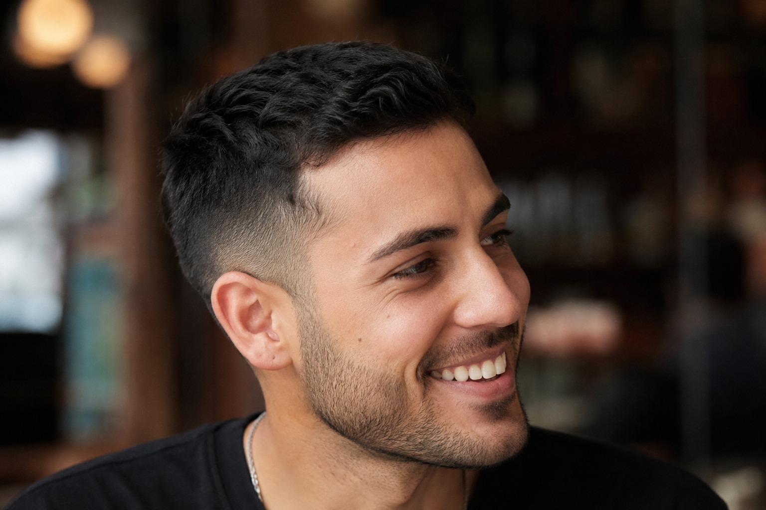 Smiling man with a clean fade and short textured hairstyle in warm indoor light.