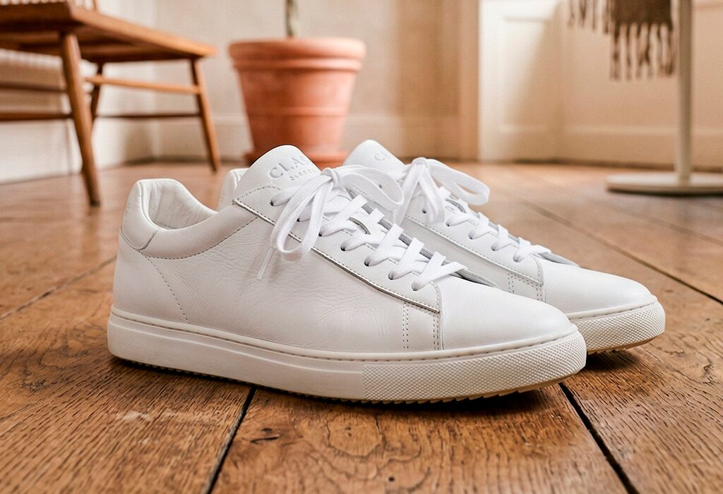Clean white leather sneakers placed on wooden floor for versatile travel packing