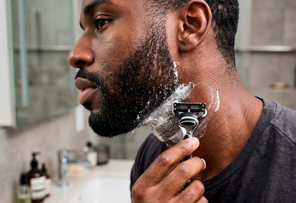 Man shaves the neck under his beard with a razor and shaving cream in a bathroom.