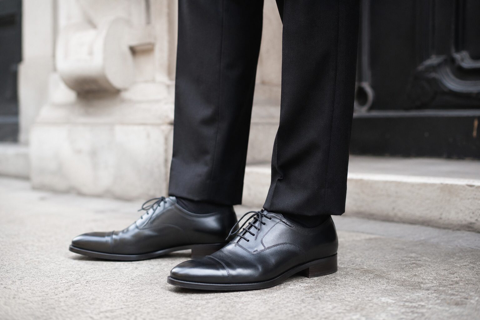 lose-up of polished black cap-toe Oxfords with slight heel, black trousers, and socks.
