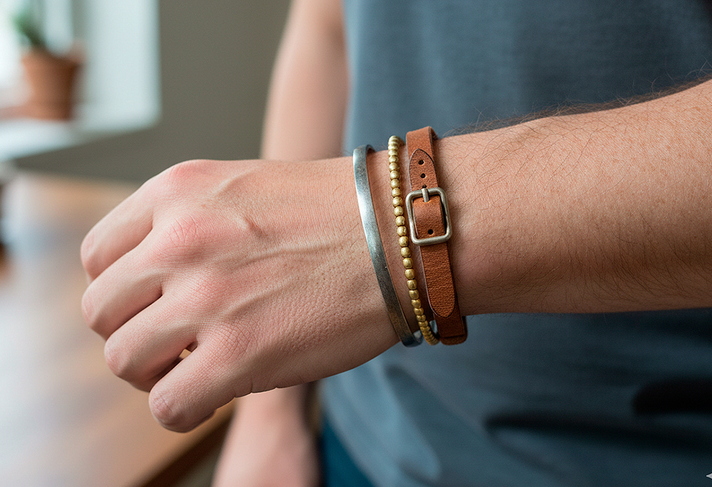 Man’s wrist wearing stacked silver cuff, gold beads, and leather bracelet trio