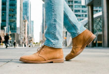 Tan suede chukka boots with light-wash slim jeans, walking through a modern downtown street
