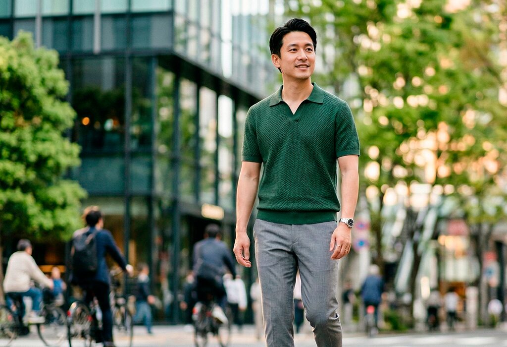 Man in dark green knitted polo and grey trousers showing polished casual spring style.