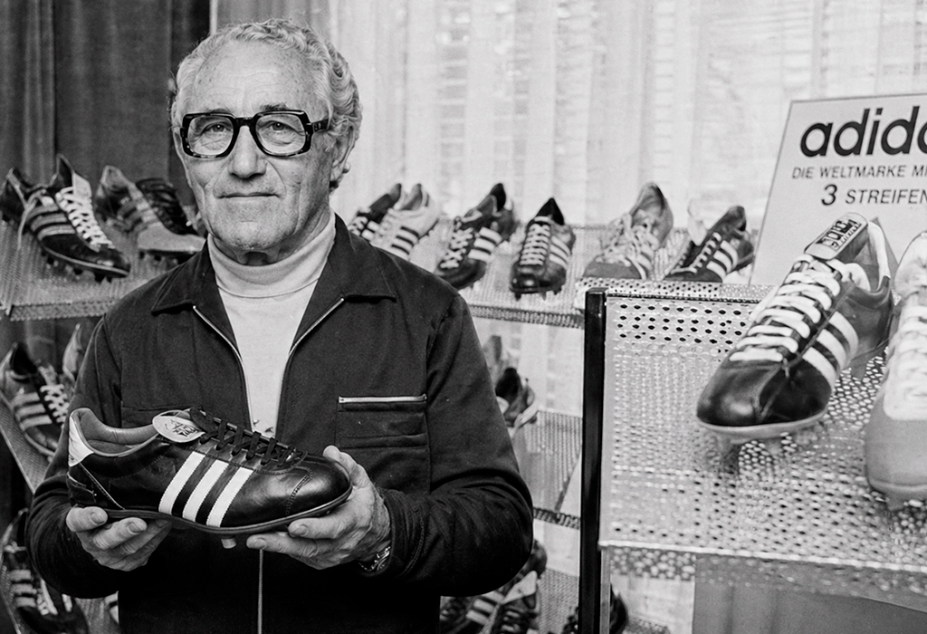 Black and white portrait of an older man holding an early three-striped Adidas football boot.