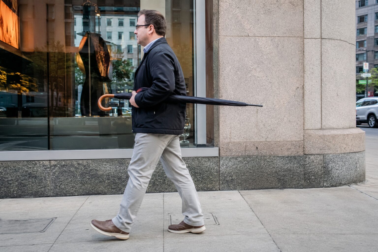 Man walks with umbrella tucked horizontally under his arm, point sticking behind him.