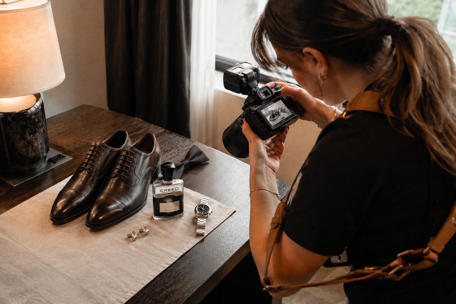 Wedding photographer capturing groom's shoes, watch, fragrance, and accessories flat lay