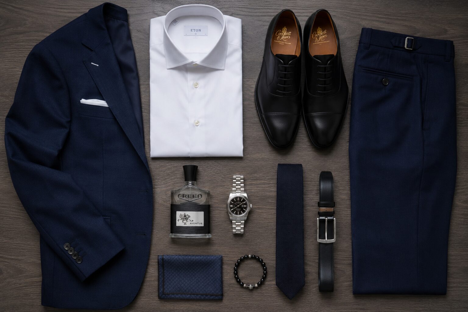 Navy suit flat lay with dress shirt, black Oxfords, watch, tie, and accessories.