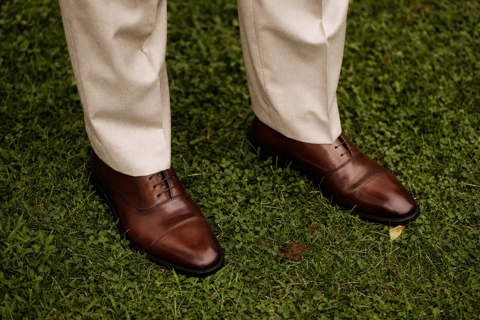 Detail shot of a man's brown leather Allen Edmonds-style oxford shoes, brown leather belt