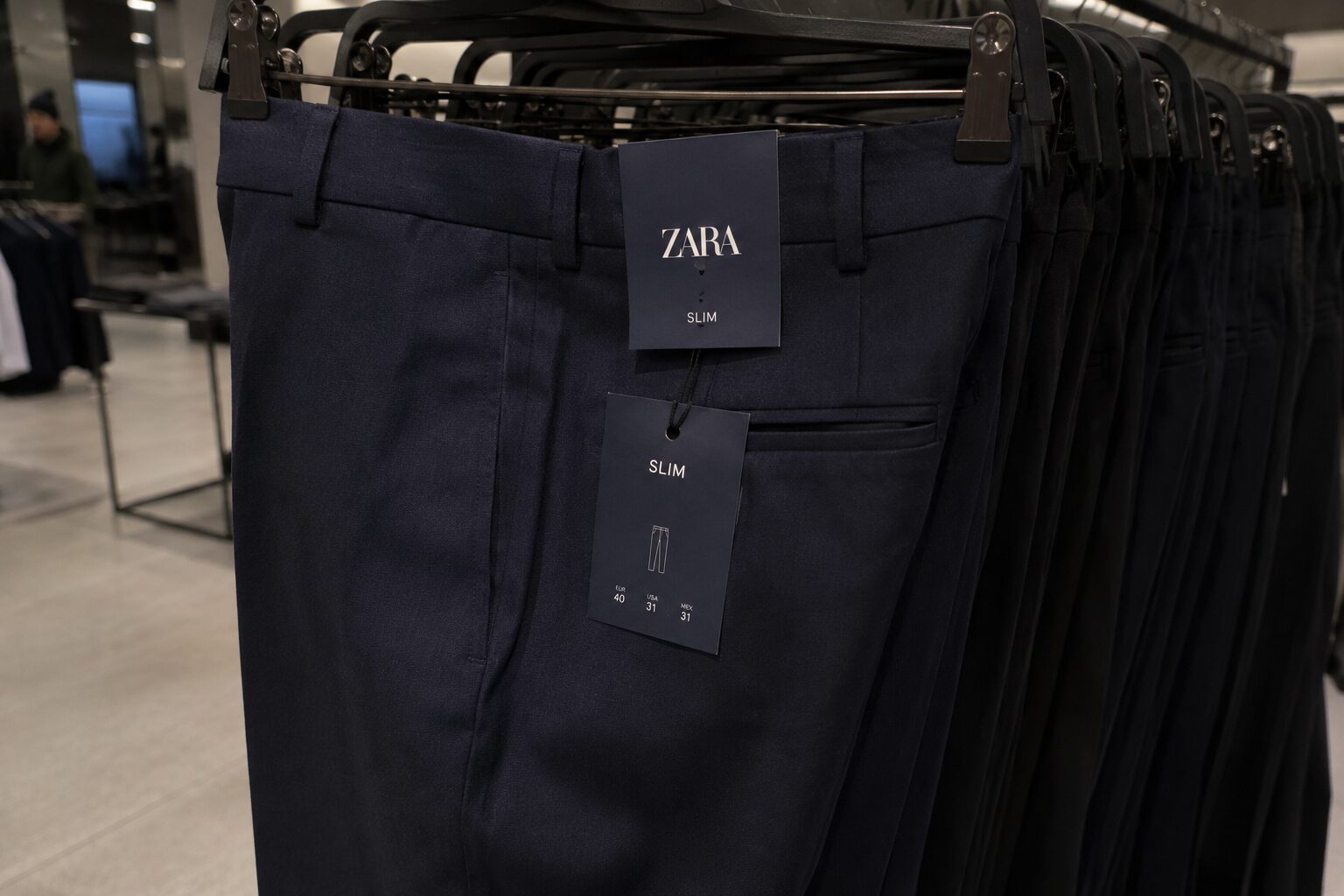 Close-up of navy slim-fit trousers on retail rack with visible brand tag.