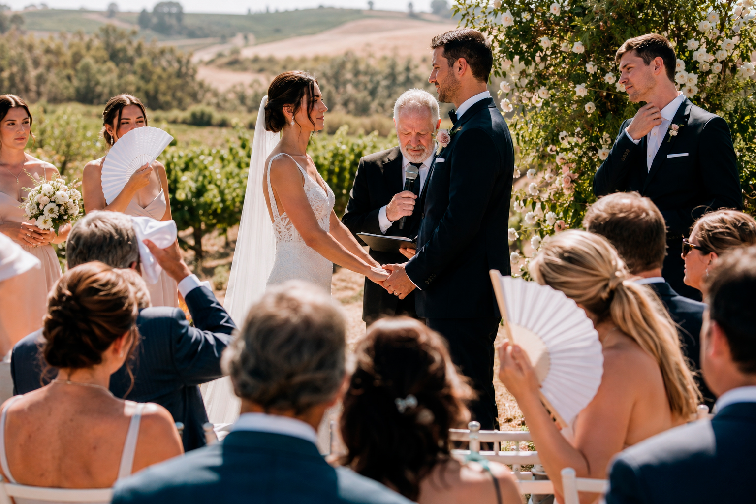 Summer Heat Wedding: Outdoor summer wedding guests use fans as groom stays composed in dark suit.
